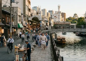 AI-generated photograph-style image of sumo wrestlers walking beside an Osaka canal, food market and traditional urban neighbourhood.