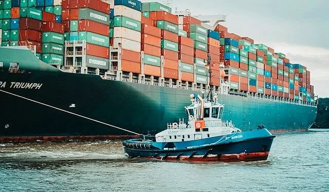 Supply Chain Resilience. Small tub boat pulling a large container ship. Photo by Mika Baumeister. Unsplash.