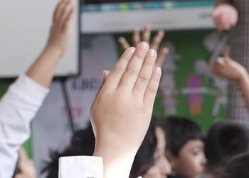 School children raising their hands in class. Photo by Department of Education. Gov.uk.