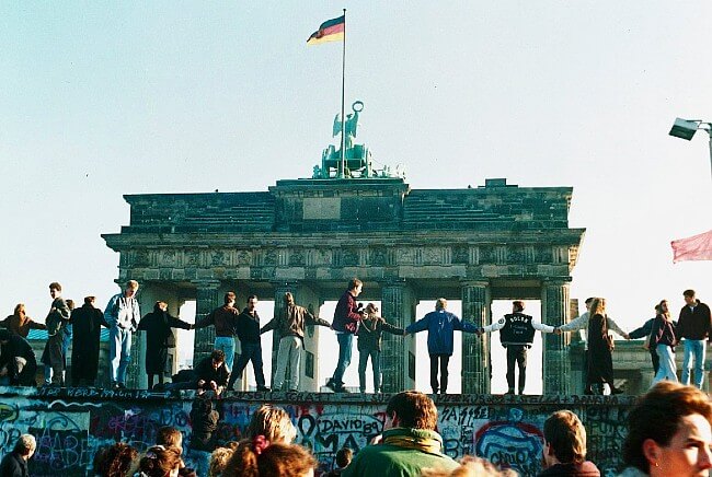 Germans stand atop the Berlin Wall in 1989. Photo by NATO. DOD.