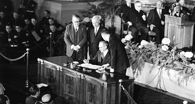 President Harry S. Truman and Vice President Alben Barkley watch as Secretary of State Dean Acheson signs the Washington Treaty on April 4, 1949. Photo by National Archives. DOD.