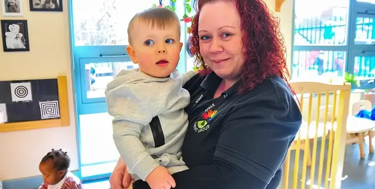 Female early years practitioner holding a toddler in her arms. Photo by Ofsted.