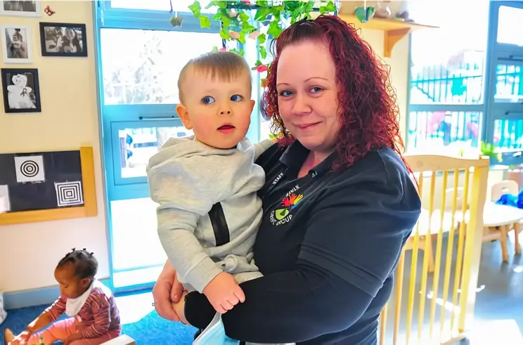 Female early years practitioner holding a toddler in her arms. Photo by Ofsted.