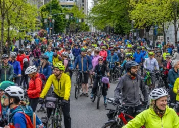 Large crowd of cyclists and electric bicycle riders gathering on a tree-lined street in downtown Portland.