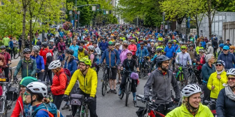 Large crowd of cyclists and electric bicycle riders gathering on a tree-lined street in downtown Portland.