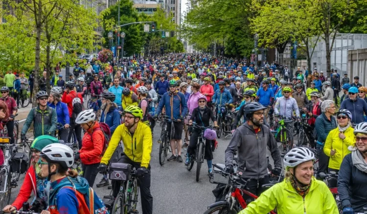 Large crowd of cyclists and electric bicycle riders gathering on a tree-lined street in downtown Portland.